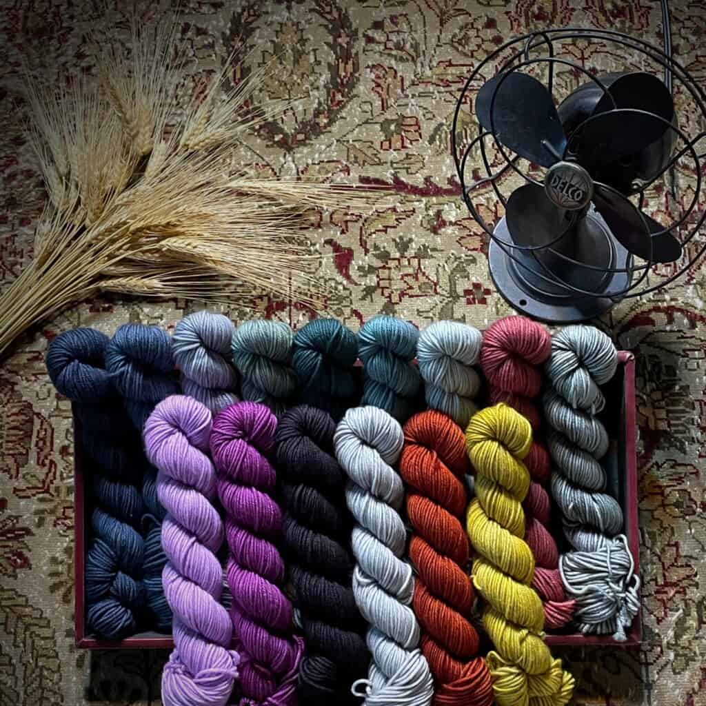Small skeins of colorful yarn in two rows next to a black fan.