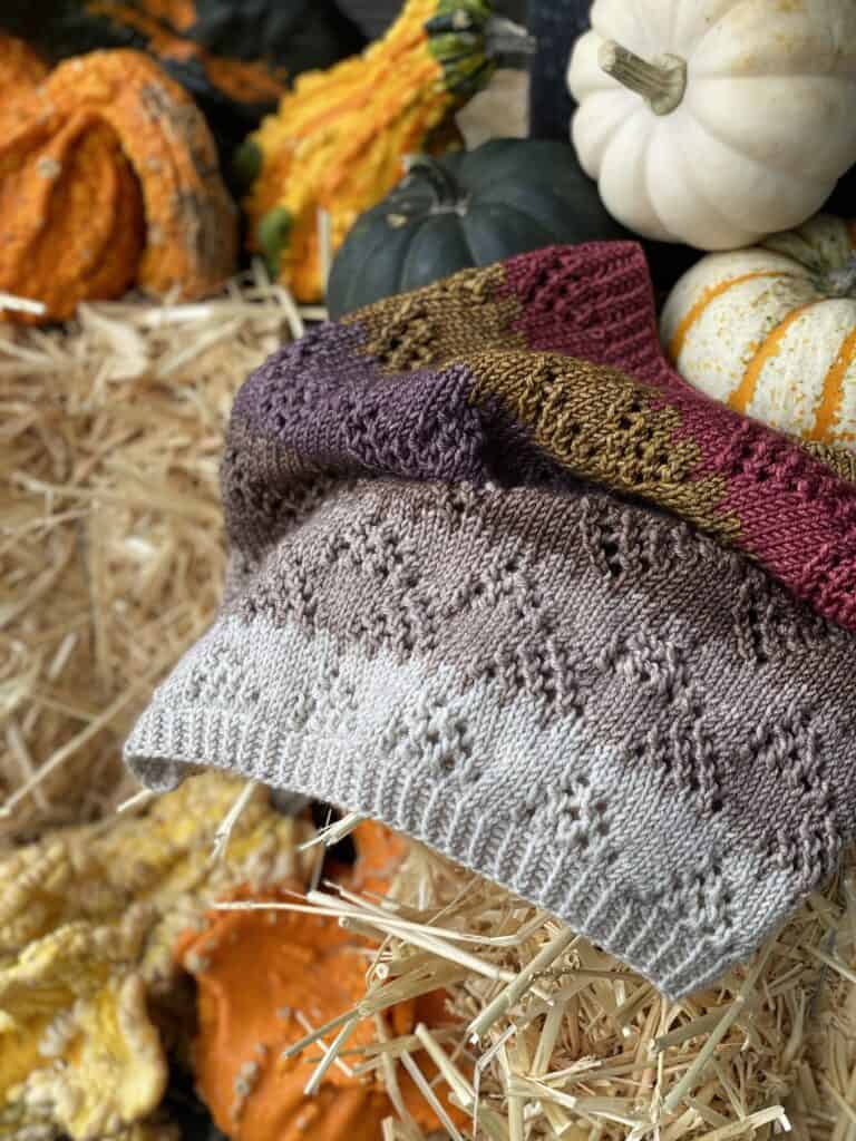 A lacy cowl with gray, brown and red stripes with mini pumpkins.