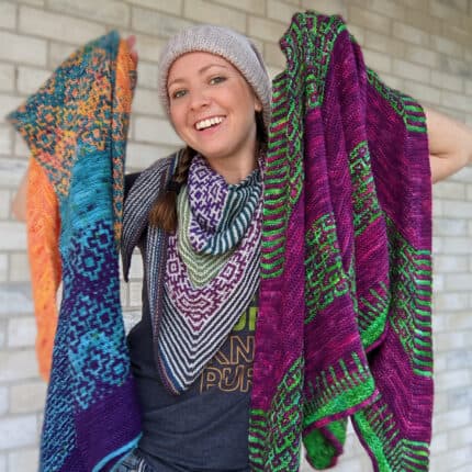 A light-skinned woman holds up multicolored shawls.