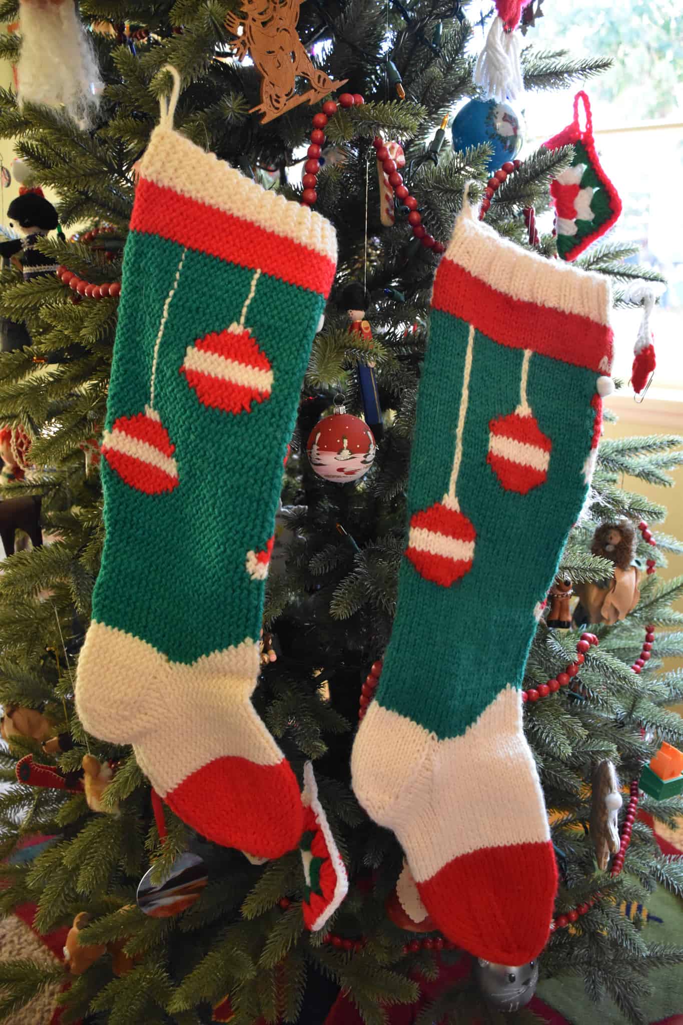 Green and red knitted Christmas stockings with tree ornaments.