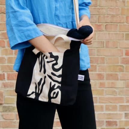 A white woman holding a natural colored tote bag with a black print.