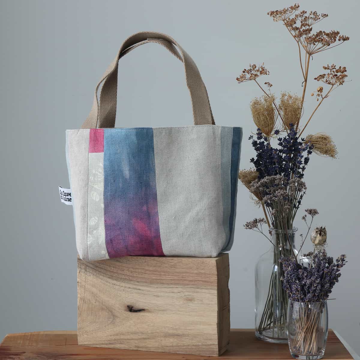 A white linen tote bag with a panel of blue and purple fabric.