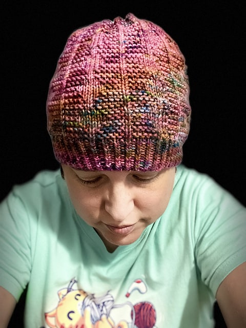 A white woman wears a pink, orange and blue speckled hat.
