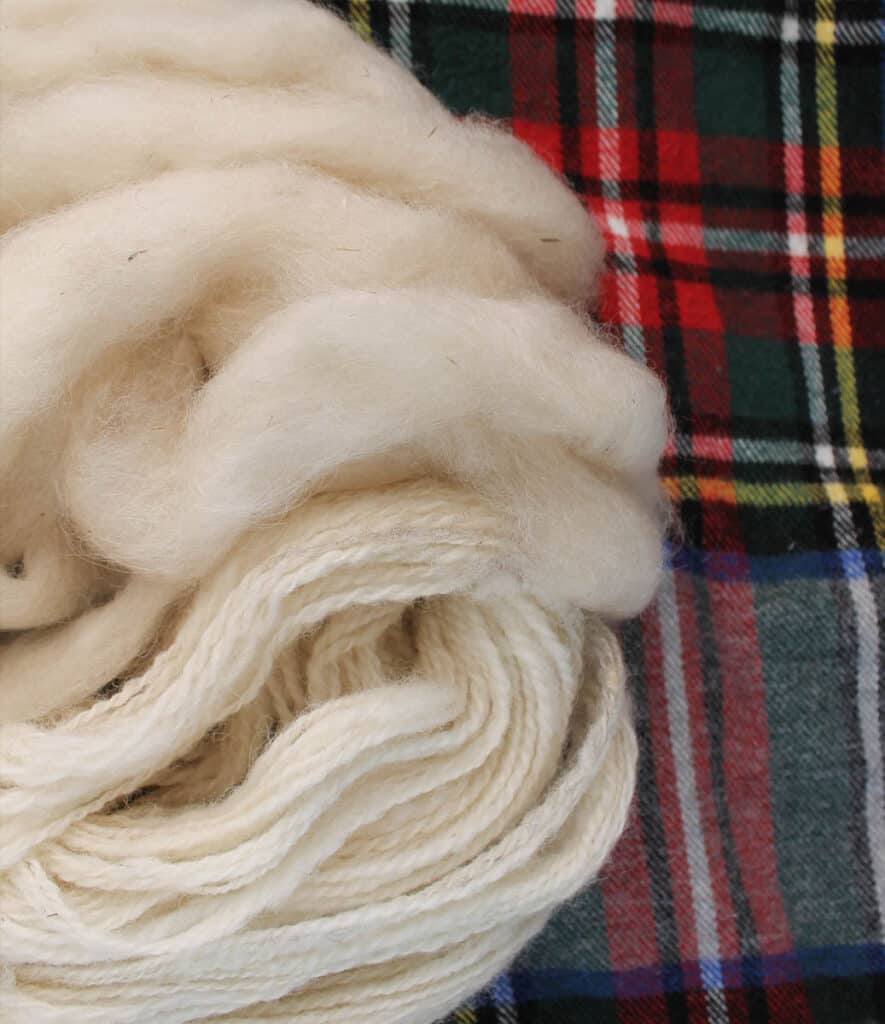 White roving and yarn sits on red, green and yellow plaid.