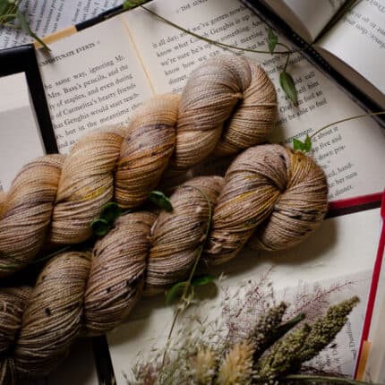 Two tan with blue green and grey speckles skeins of yarn resting on open books.