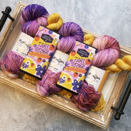 Pink and purple speckled yarn with lemon yellow mini skeins and a matching chocolate bar.
