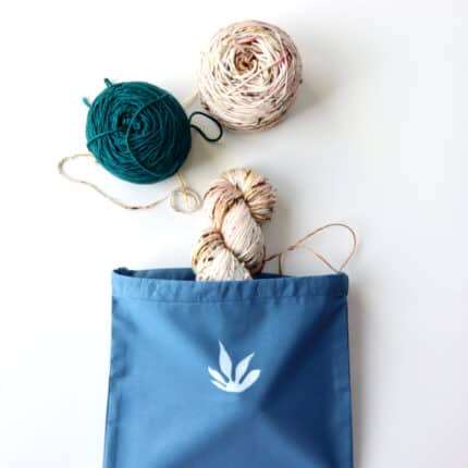 A blue drawstring bag with teal and pink speckled yarn coming out of it.