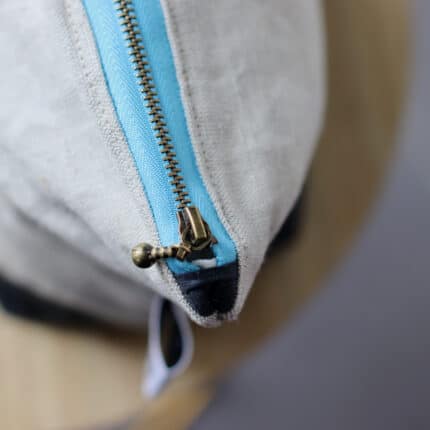 A close up of a gray bag and its pale blue zipper.