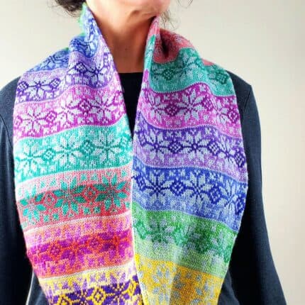 A multi-colored fair isle star pattern infinity cowl draped over a person's neck set against a charcoal-colored shirt.