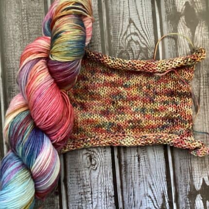 A skein of yarn in blues, yellows and reds and a knitted swatch in the same colors.
