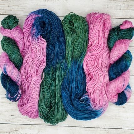 Two open skeins of yarn between two twisted skeins each containing shades of pink, blue, and green.