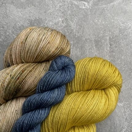 Two skeins of yarn, one natural and speckle and one ochre, with a small blue mini skein.