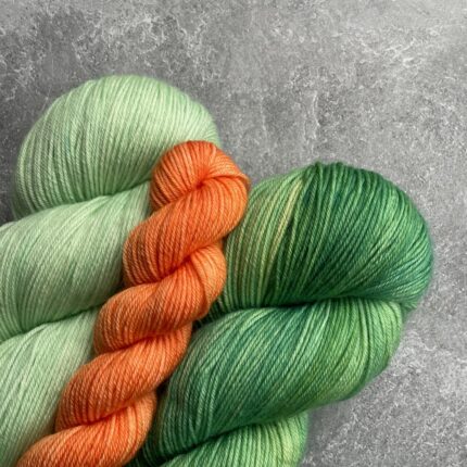 Two green skeins of yarn, one light and one dark, with a small orange mini skein.