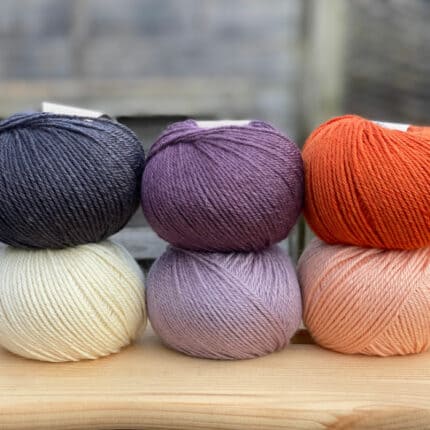 Six balls of yarn in white, black, purples and oranges.