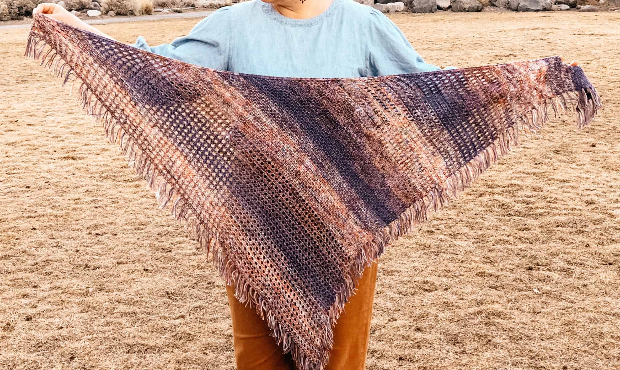 A textured and eyelet shawl with fringe in orange, purple and blue faded yarn.