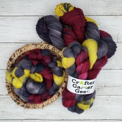 Two skeins of yarn and two braids of fiber containing shades of burgundy, dark grey, black, and yellow.