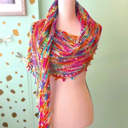 A shawl in a pink, purple, blue and orange variegated colorway displayed on a dress form.