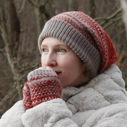 A light-skinned model wearing a slouchy patterned hat and fingerless mitts in red and gray.