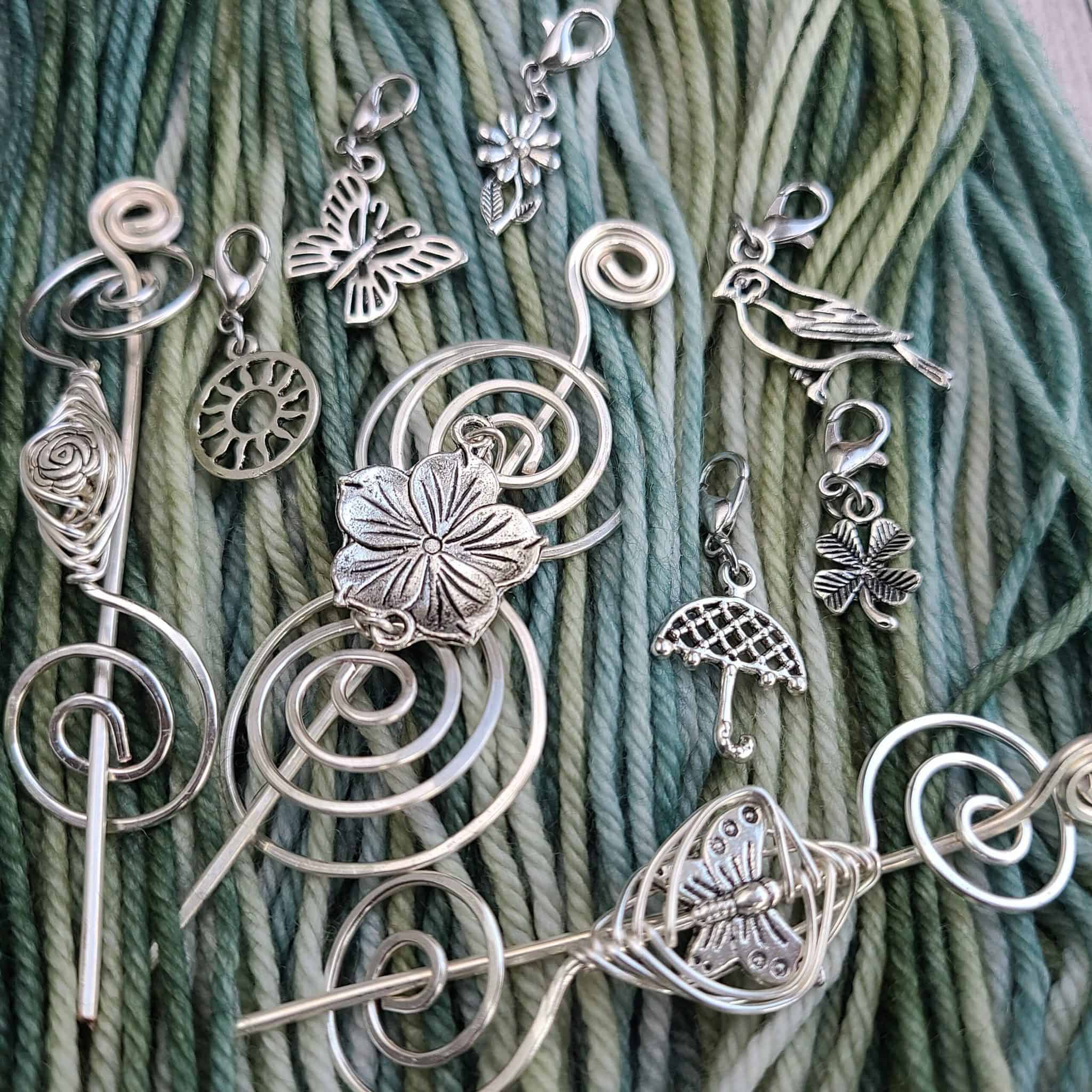 Silver metal shawl pins and stitch markers on a background of blue-green yarn.