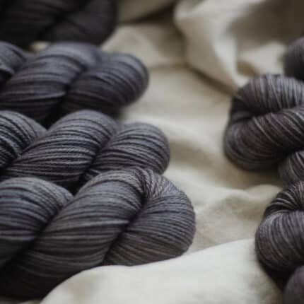 A pile of warm charcoal yarn laying on a linen fabric.