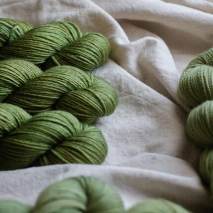 A pile of green tonal yarn laying on a linen fabric.