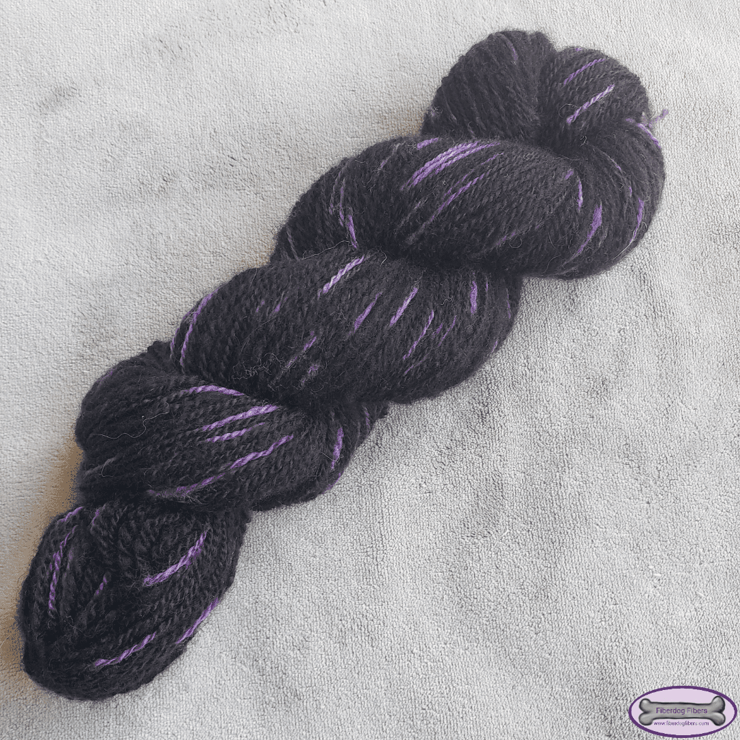 A mostly black skein of yarn with purple spots on a grey background.