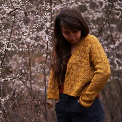 A light-skinned woman wearing a yellow cardigan in the woods.