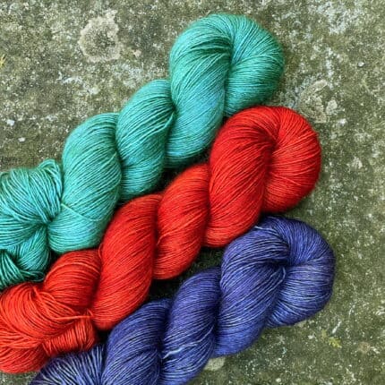 P Three skeins of yarn, in green-blue, orange and purple yarn on a granite slab.