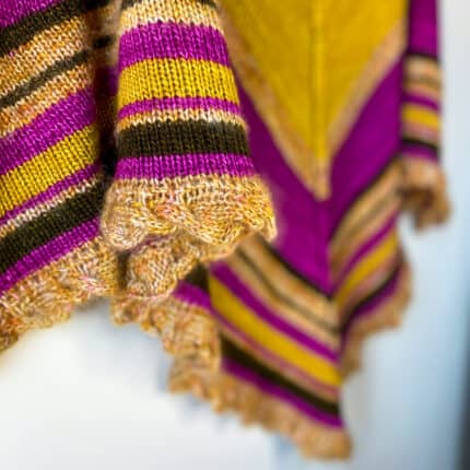 Close-up of a cable border and stripes of a triangular shawl in magenta, brown, and gold.