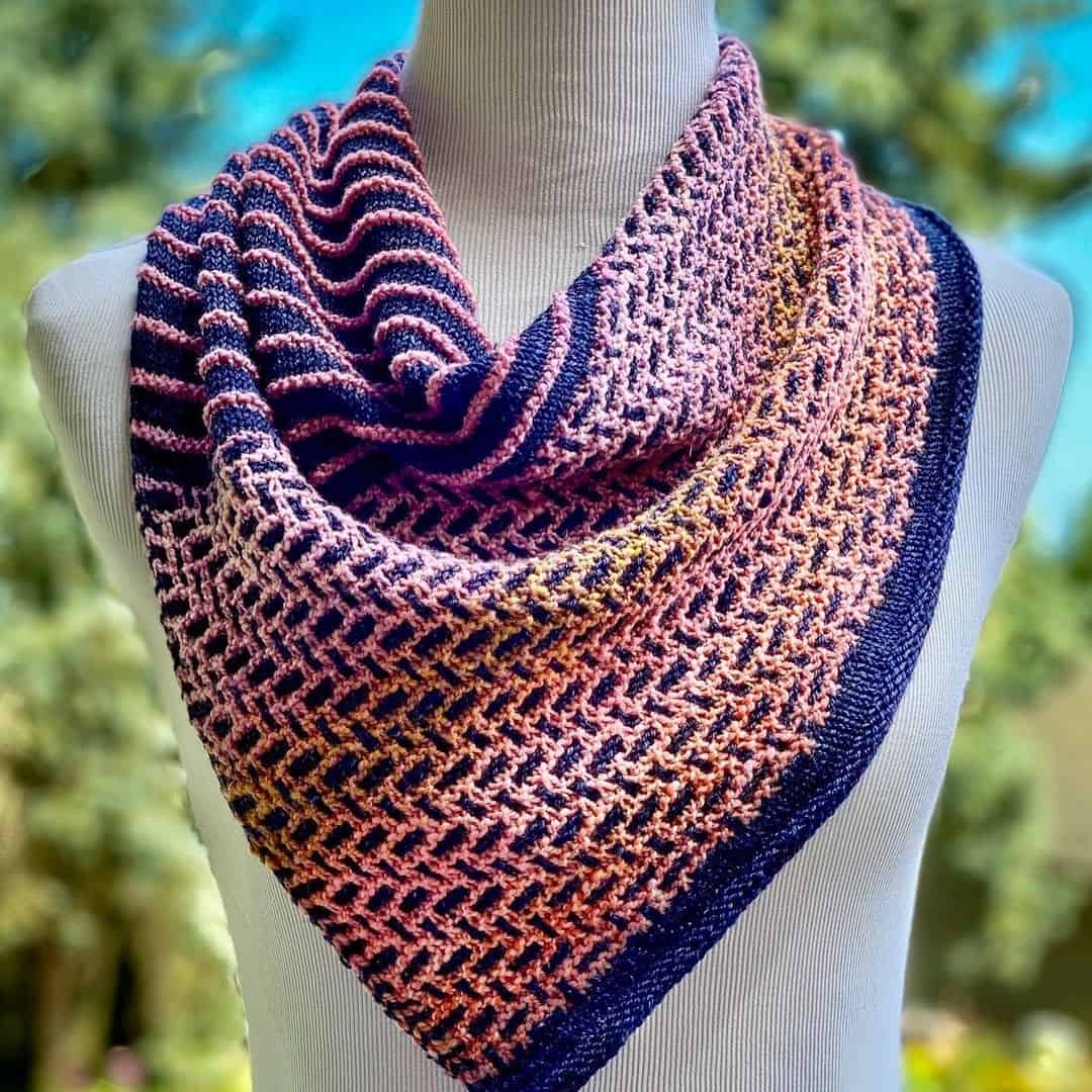 A triangular cowl in blue and light pink sitting on the neck of a dress form. 