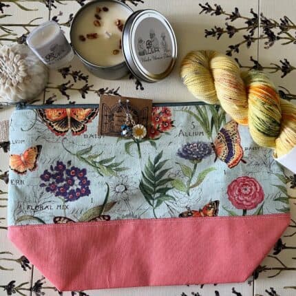 A flower shaped soap, a lotion bar, bird and flower charms, yellow yarn skein with speckles and a floral bag with butterflies.