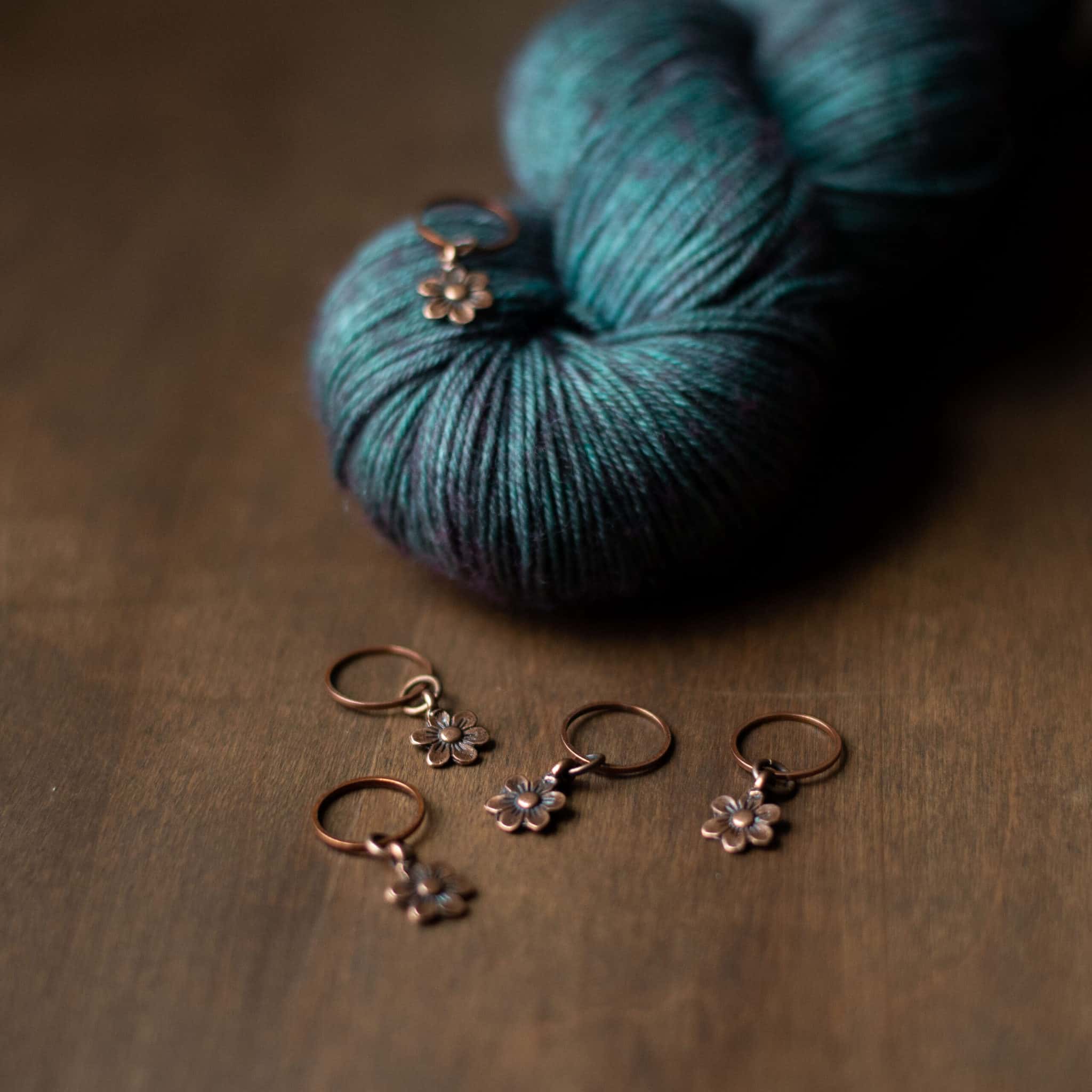 Copper daisy stitch markers on a skein of teal yarn.