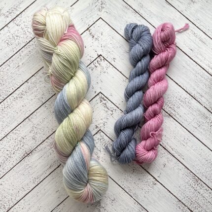 A skein of yarn in blues and pinks with two mini skeins in blue and pink.