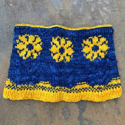 A blue knit cowl with cables and yellow flowers.