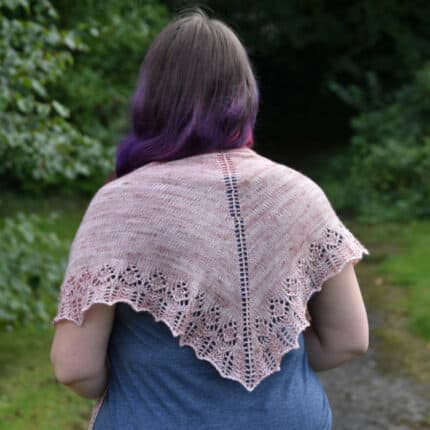 A light-skinned woman shown from the back wearing a pink triangular lace-edged shawl.