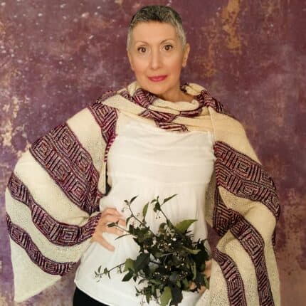 A light-skinned woman wearing a big stole in white and purple. She is holding a bouquet of wildflowers.