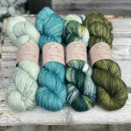 Four skeins of yarn in shades of green and blue.