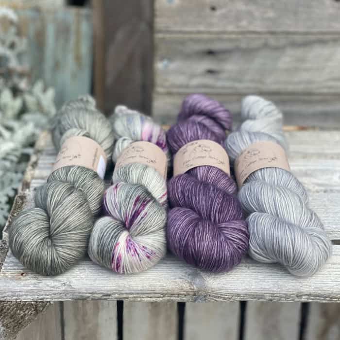 Four skeins of yarn in shades of grey and purple.