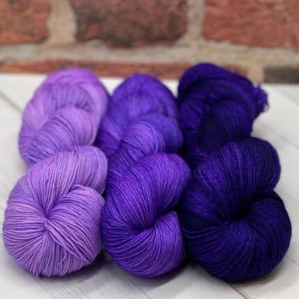 Three skeins of yarn in various shades of purple.