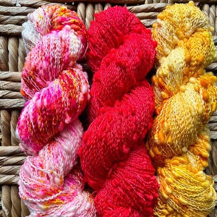 A trio of skeins of yarn with slubs in a bright speckled red, pink and orange.