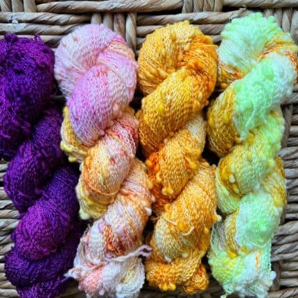 Purple, variegated pink and yellow, orange and brightly colored sun yellow skeins in a slubby yarn with texture.