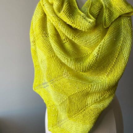 Bright lemon yellow shawl draped around mannequin showing off garter and chevron stitches with fingering and suri yarn.