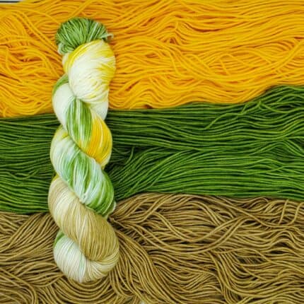 A splashy variegated skein of yarn atop semisolid skeins of warm yellow, vibrant green, and a light earthy brown.