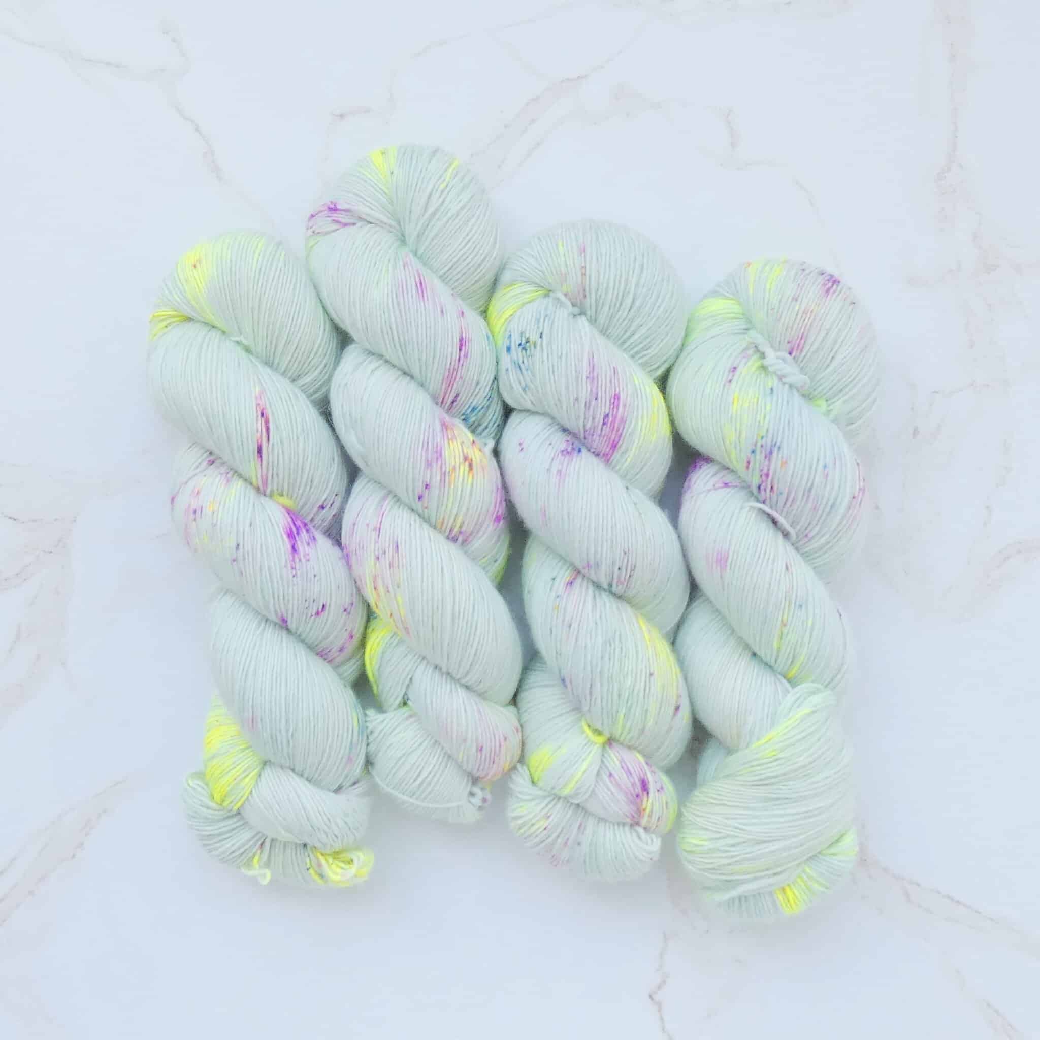 A pastel sage yarn speckled with pops of neon yellow and pink and deep green.