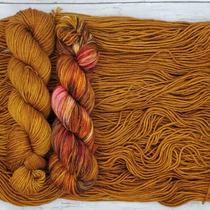 A variegated skein of of warm hues and earth tones atop and beside warm cinnamon semisold brown skeins.