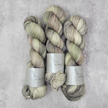 Three skeins of variegated yarn layered with khaki green, tans and cream.