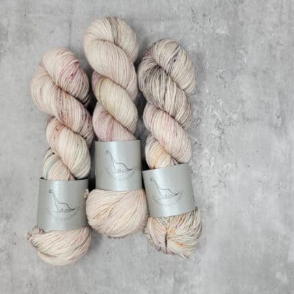 Three skeins of soft cream yarn with soft speckles of orange, pink and brown.