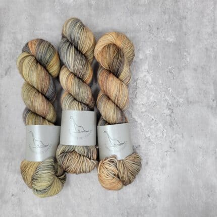 Three skeins of variegated yarn with layers of dusty yellow, persimmon, jeans blue and sand.