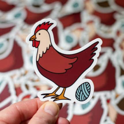 A sticker of a dark red chicken laying a yarn ball egg.