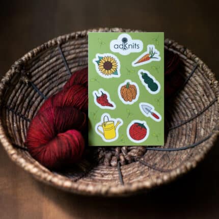 A garden-themed sticker sheet sits in a woven basket with a hank of red yarn.